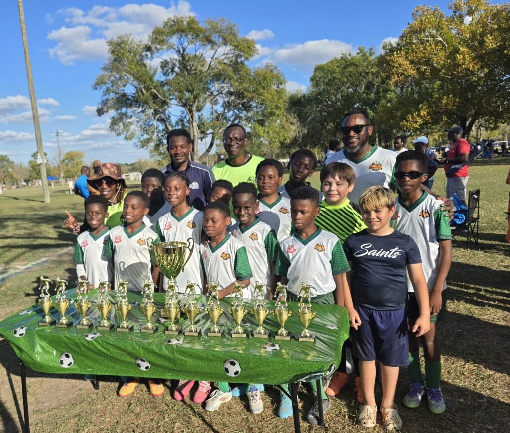 A Redeemer Sports youth soccer team gathered with coaches and trophies after a game